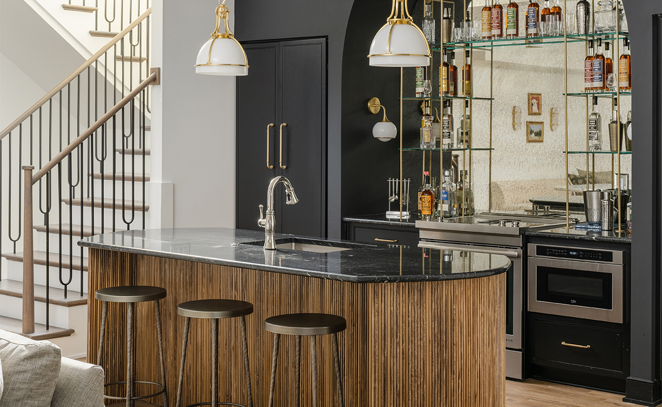 Dark and moody wet bar space in a basement entertainment room featuring black painted cabinets and glass shelving.