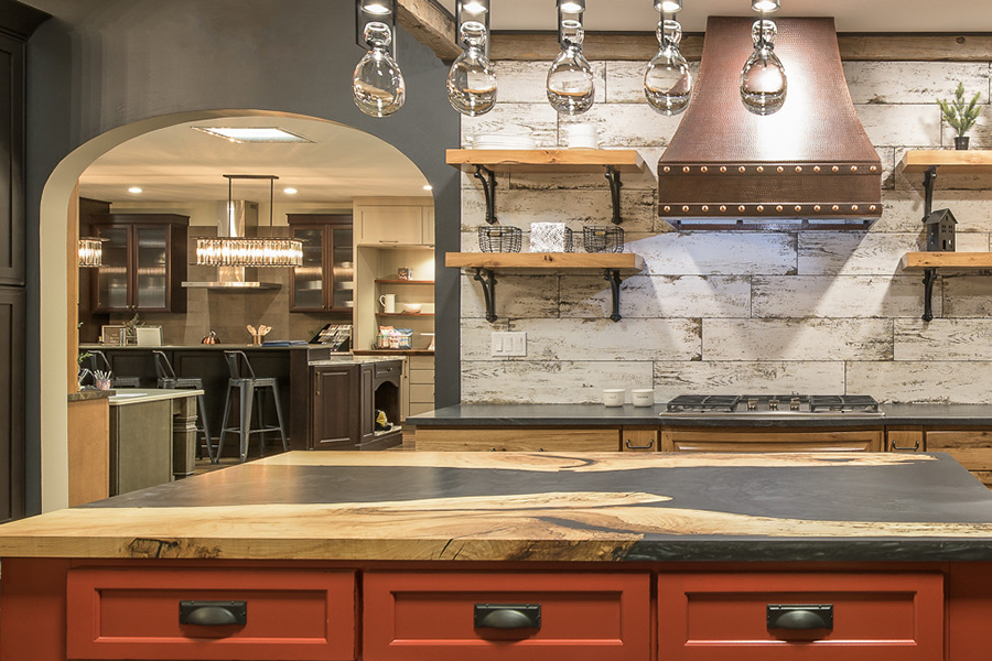 A traditional farmhouse kitchen display with rustic details in a Bertch Cabinet showroom features a custom paint color to a barn red on the kitchen island. Find a Bertch Showroom today!