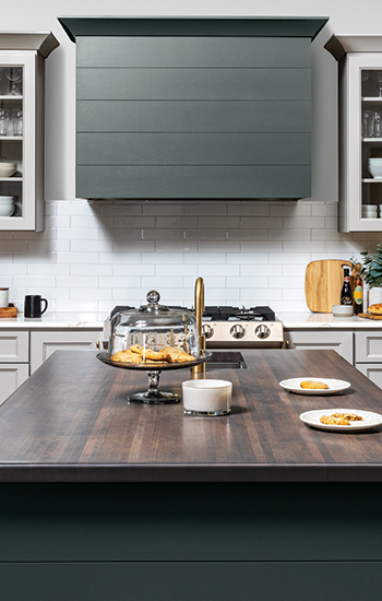 A close up of a modern wood hood with shiplap details and a hunter green painted finish surrounded by off-white, light gray cabinets with a dramatic flat panel door style.