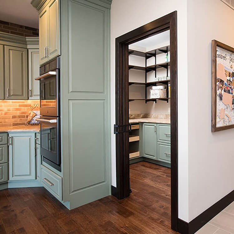 A soft, sage green and dark brown kitchen design with butler's pantry.