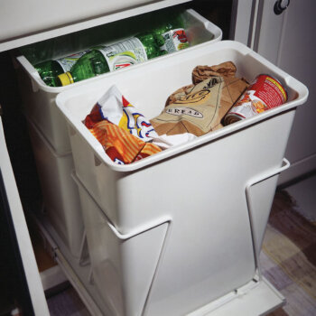 Design a kitchen with a cabinet designated for a more organized and sanitary space for the wastebasket and recycling bins. The pull-out accessory features 2 trash cans hidden behind a cabinet door.