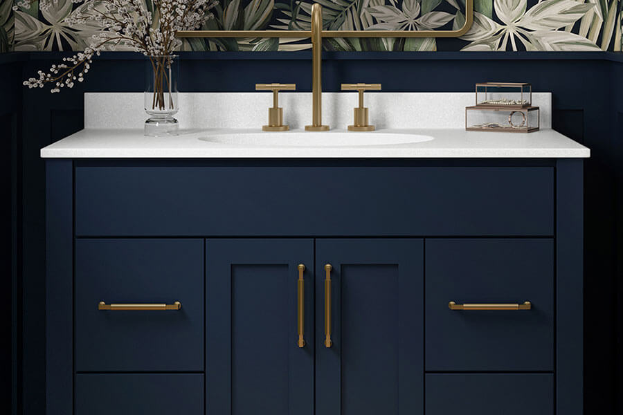 A close up of a navy blue vanity with brushed brass/gold hardware, a solid white countertop, and trendy wallpaper.