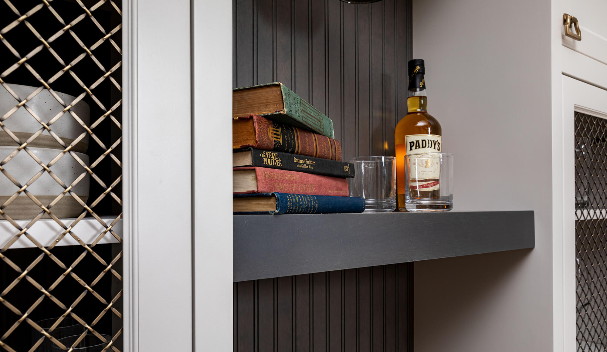 A close of the stylish details of a trendy wet bar design featuring gold wire mesh cabinet doors and a gray floating shelf.