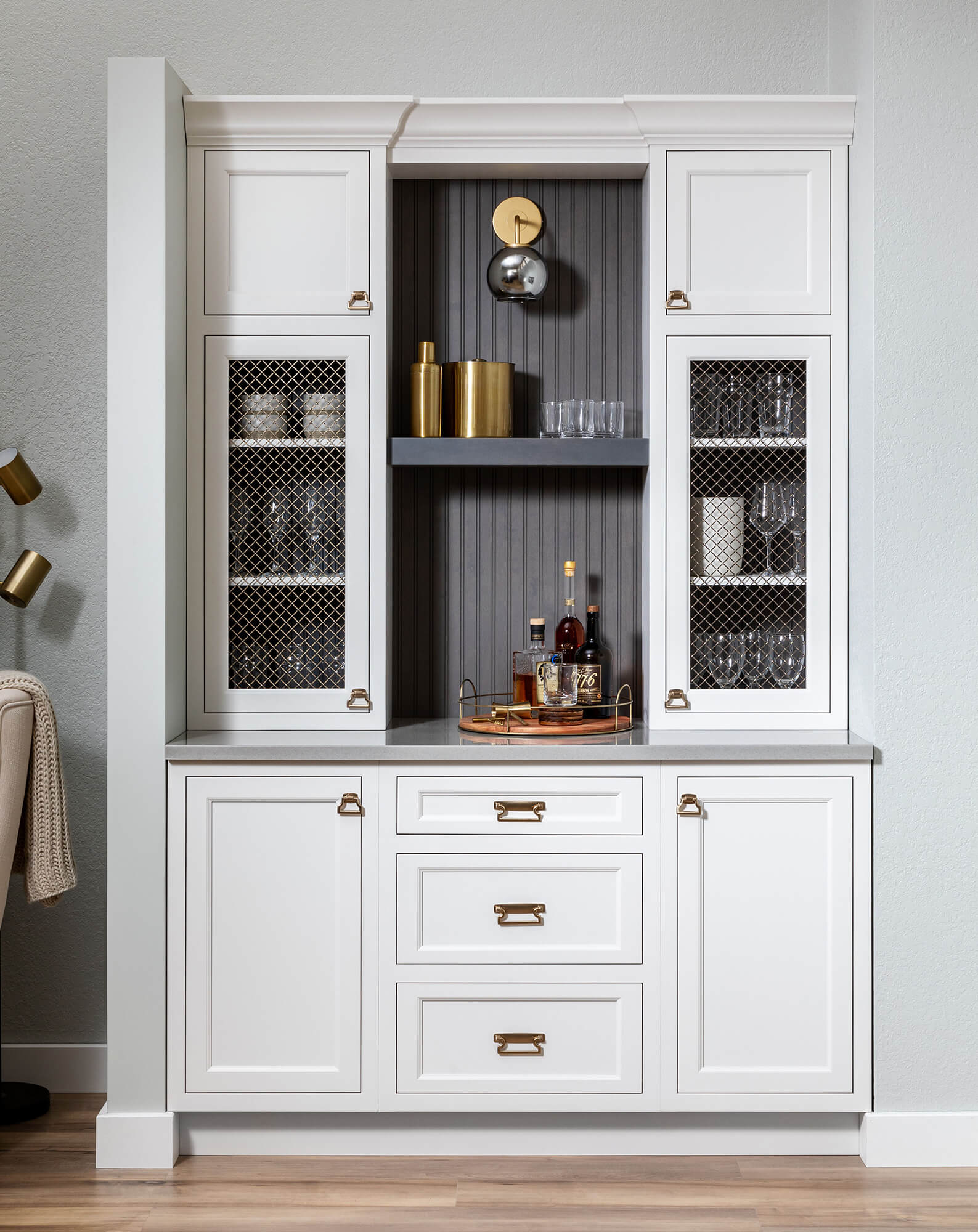 A stylish wet bar with white painted inset cabinets featuring wire mesh cabinet inserts.