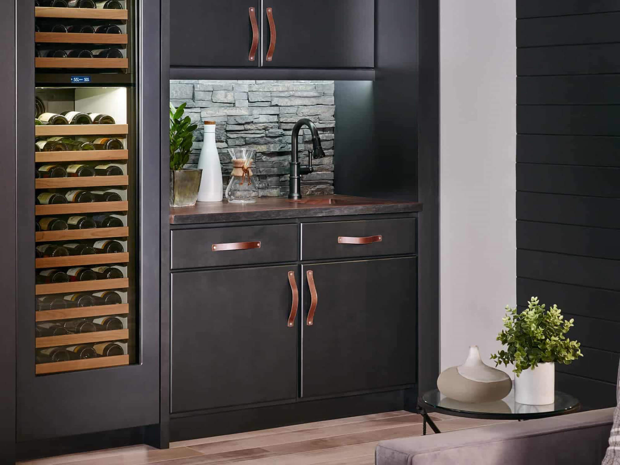 A black, contemporary wet bar space with a sink and a tall appliance paneled wine fridge featuring Bertch cabinets.