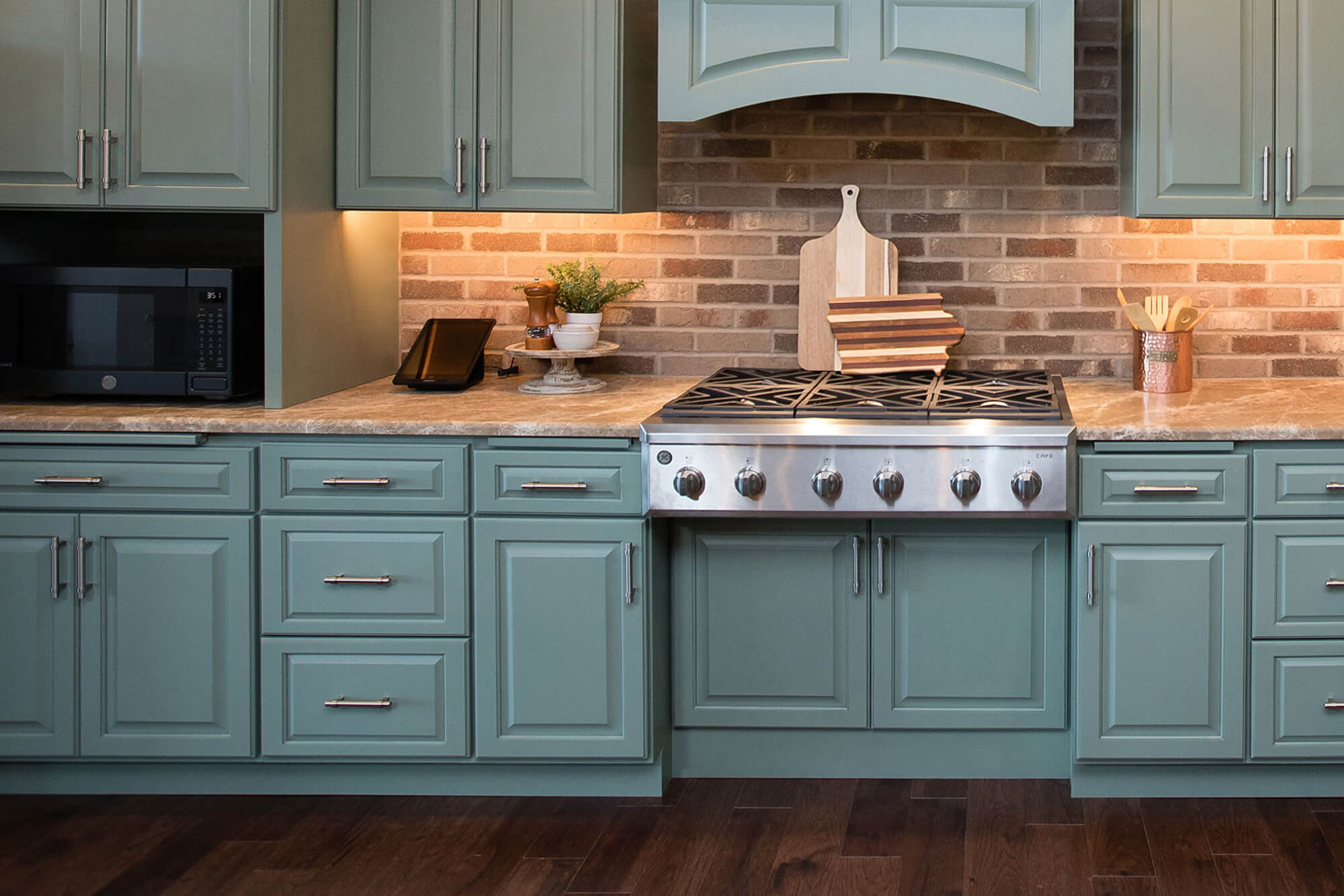 A minty green kitchen with traditional raised panel cabinet doors and nickel pulls featuring a historic looking brick wall backsplash.